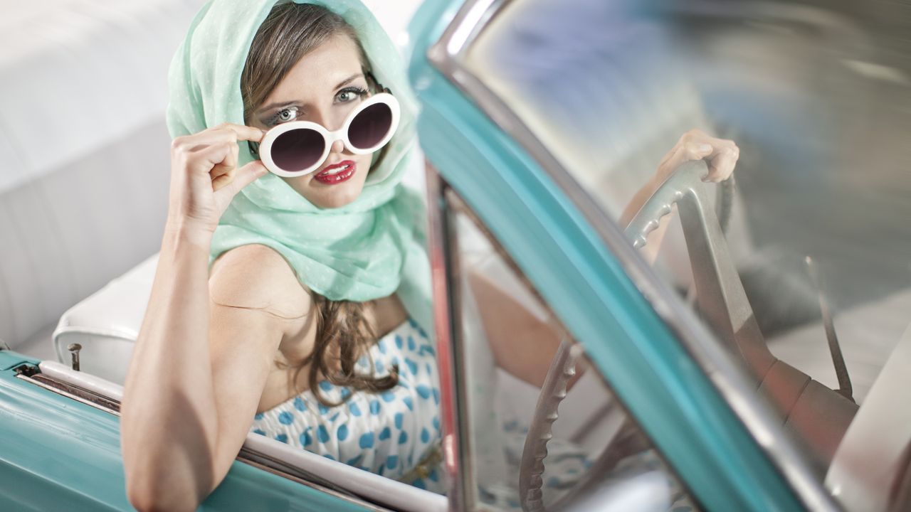 A woman in a convertible tips down her sunglasses.