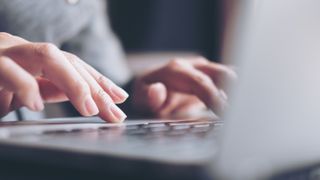 A close up photo of a person's hands typing on a laptop keyboard