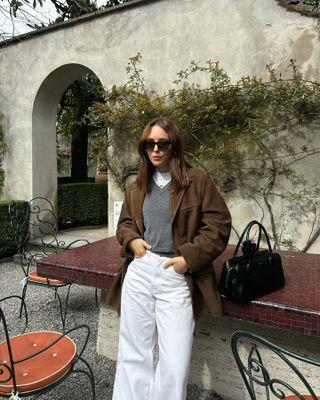 Woman wearing suede jacket, gray sweater, and white jeans.