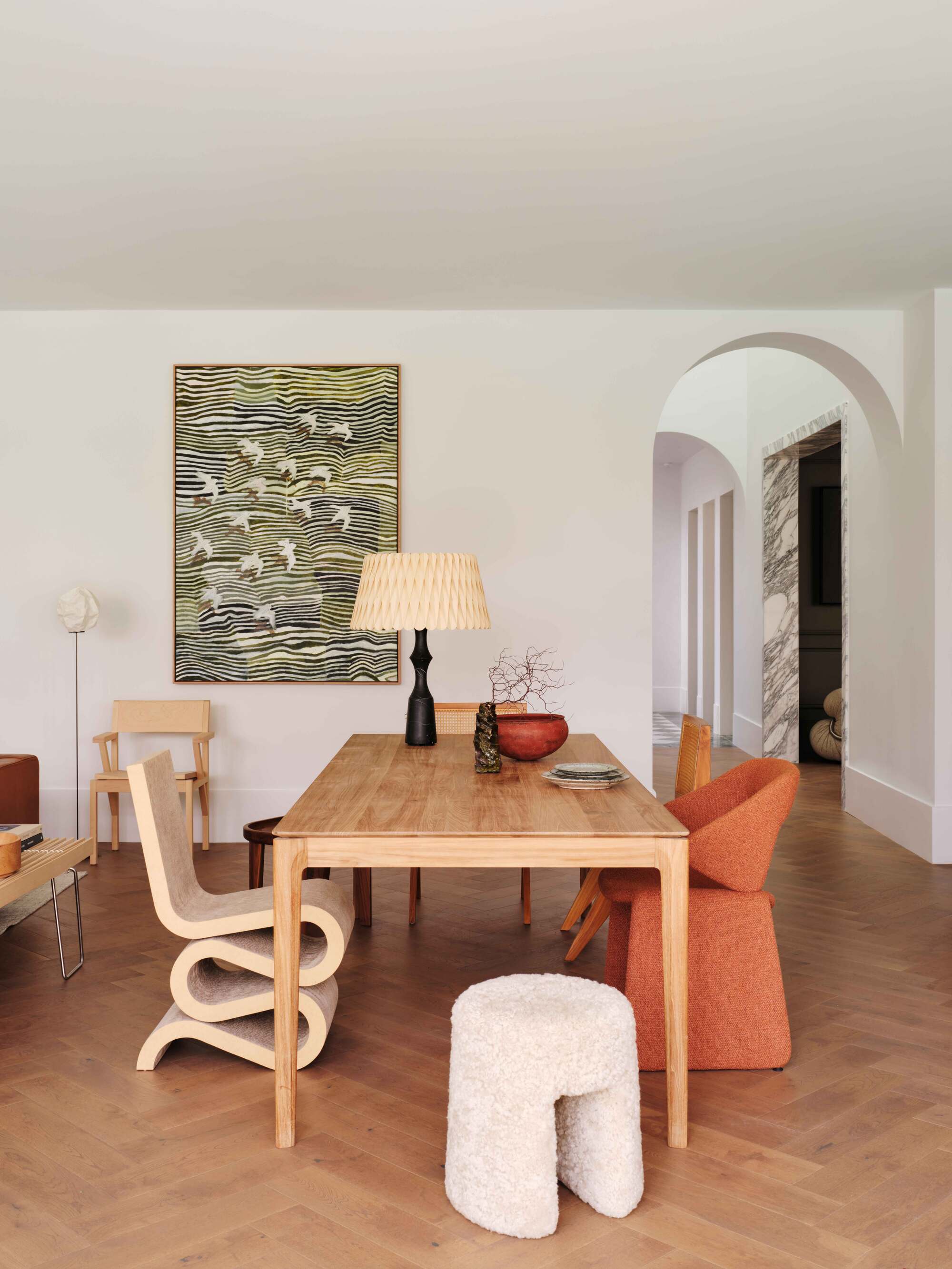 open plan room with timber table, mismatched dining chairs, parquetry floors, arched doorway leading through to the hallway, and a large artwork on the wall
