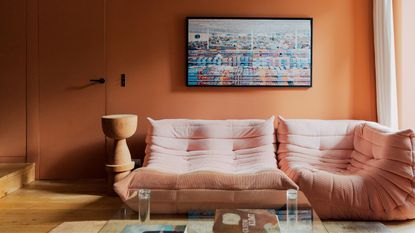 pink togo sofa in front of orange wall with artwork and glass coffee table