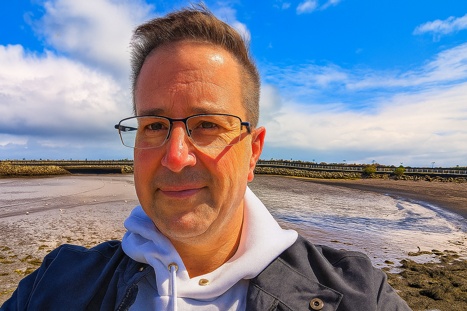 Head and shoulders selfie of Tom May on a beach, with a blue sky in the background