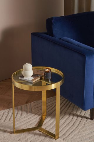 A metallic side table next to a dark blue sofa