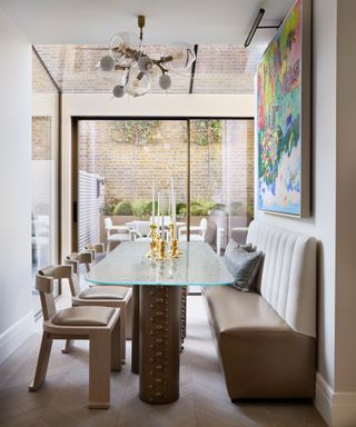 open plan kitchen dining area with taupe bench and chairs, glass table and statement colorful artwork