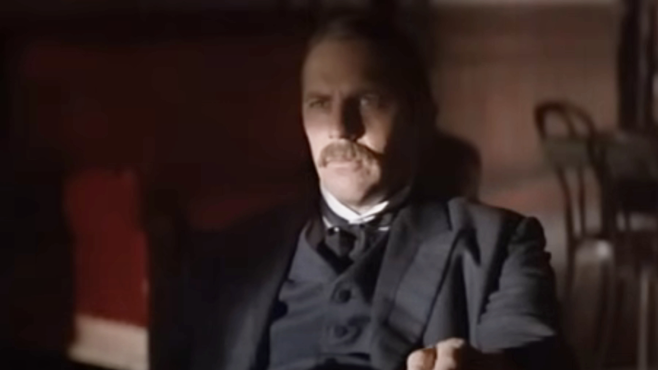 Kevin Costner as Wyatt Earp sitting at a table in Wyatt Earp