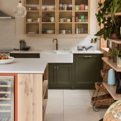 dark green and terracotta kitchen with wood panelling, white work tops, glazed wall unit, open shelving, white floor tiles