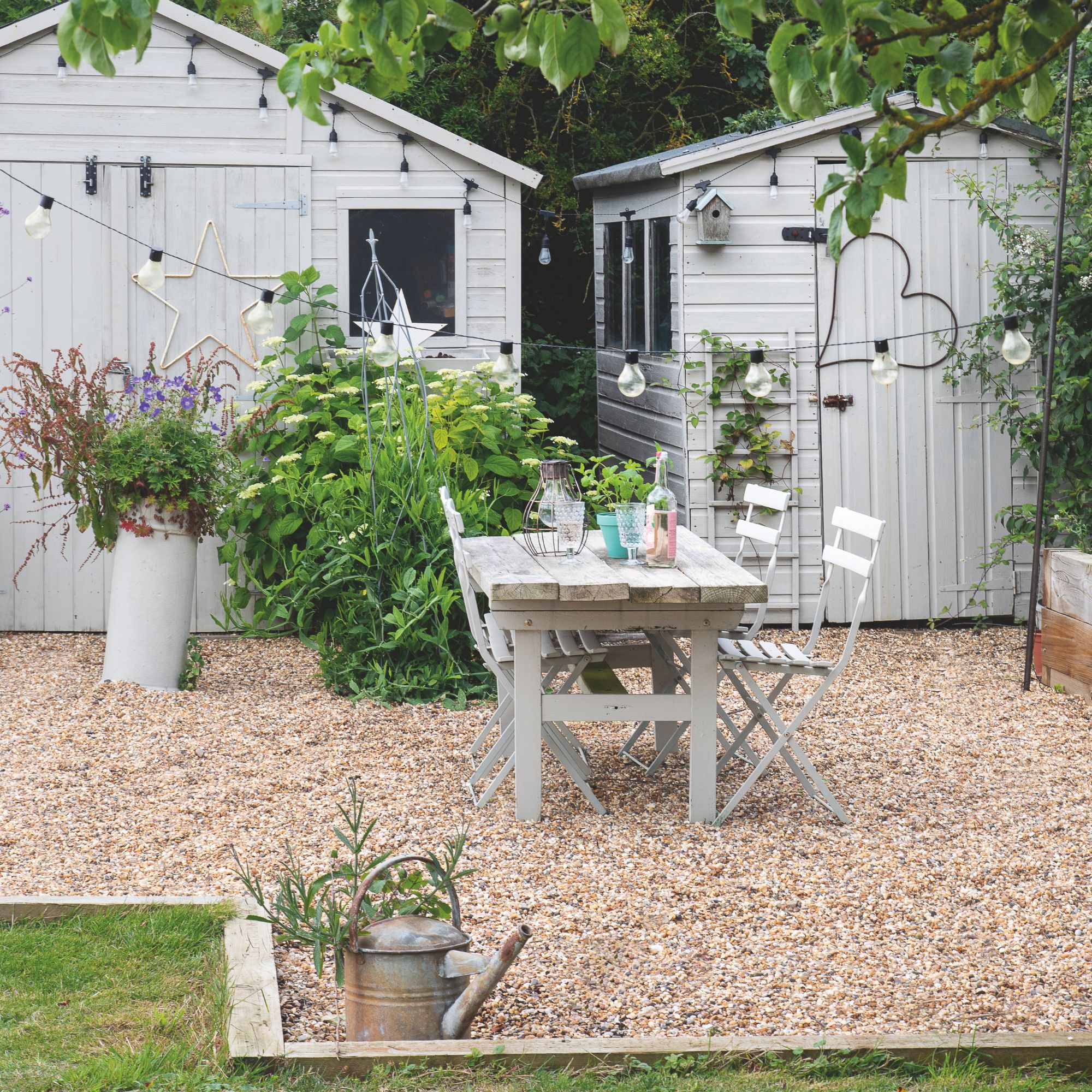 Gravel area in a garden with two grey painted sheds behind it