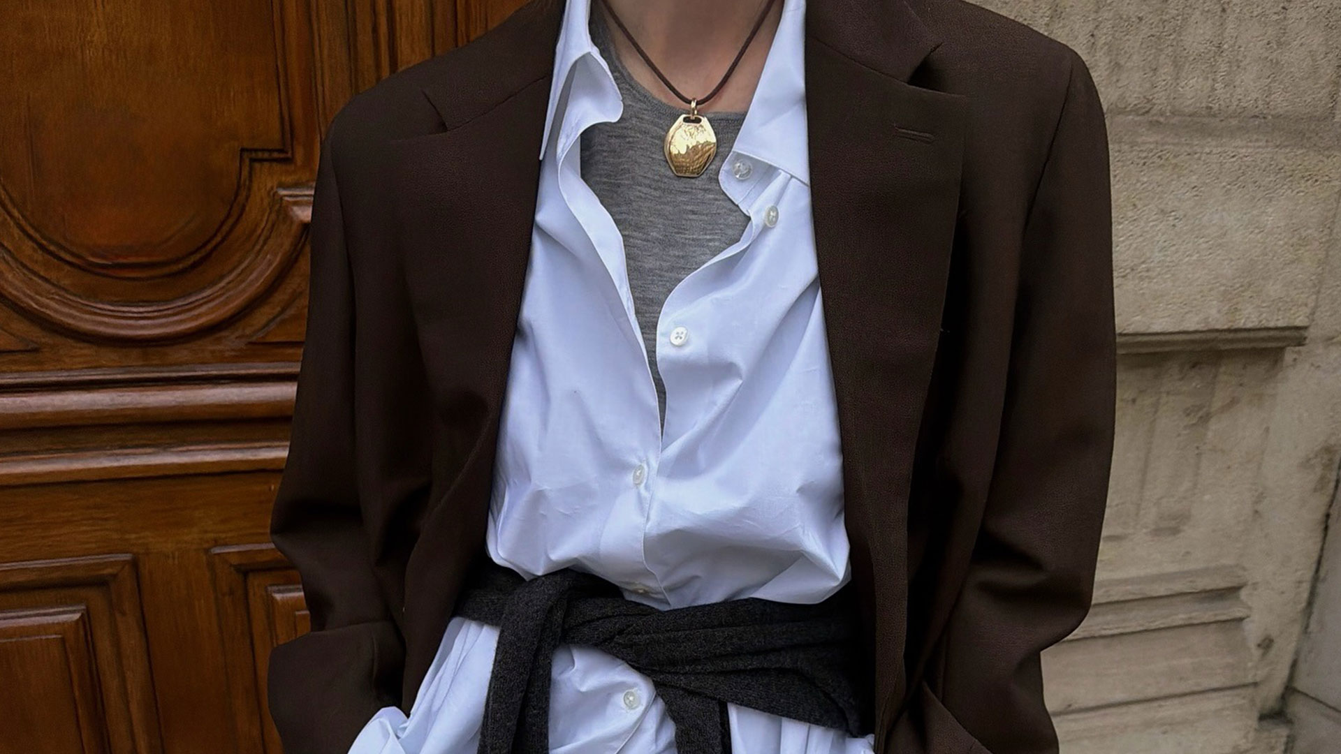 @annabelrosendahl wearing a white button down, brown blazer, gold necklace, and sweaters under and around waist.