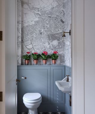 A light gray powder room with white sanitaryware and black and white map wallpaper above gray panels