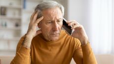 Concerned older man holds a phone to his ear