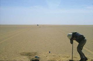 Survey line in the sand sheet north of Kiseiba Oasis, in southern Egypt. Dr. Vance Haynes is using a hand auger to determine the shallow layering in the sand and fluvial sediments.