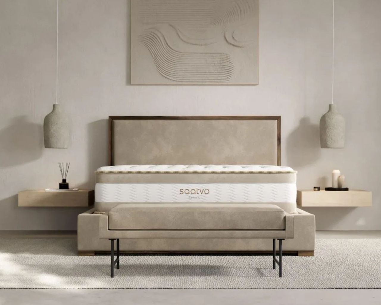 A Saatva RX mattress shown in a neutral bedroom with floating bedside shelves, a large artwork, hanging pendant lamps, and a beige bench with black legs.