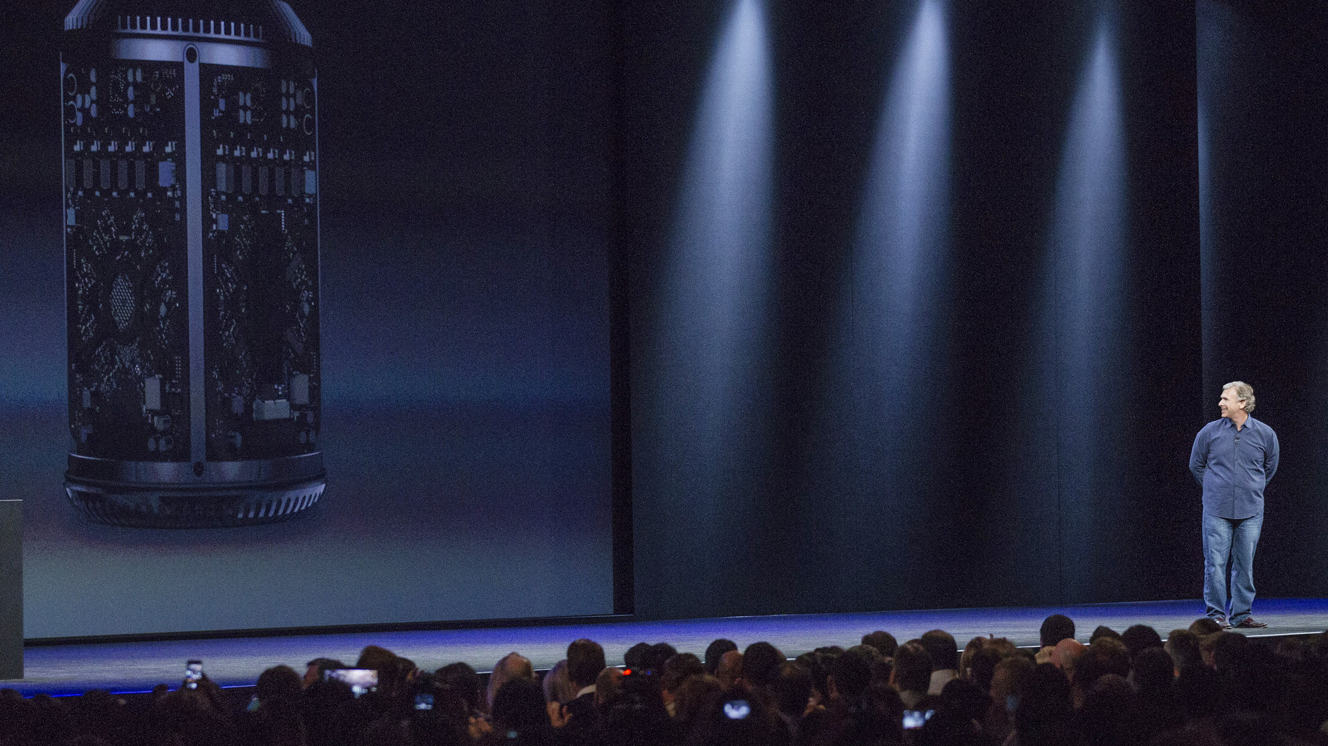 Apple's Phil Schiller on stage at WWDC 2013 looking back at an image of the new Mac Pro