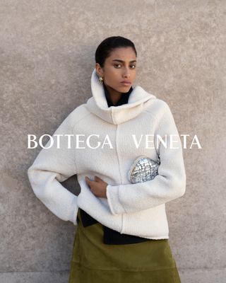 A model in a white sweater, green skirt, silver The Knot Bag by Bottega Veneta