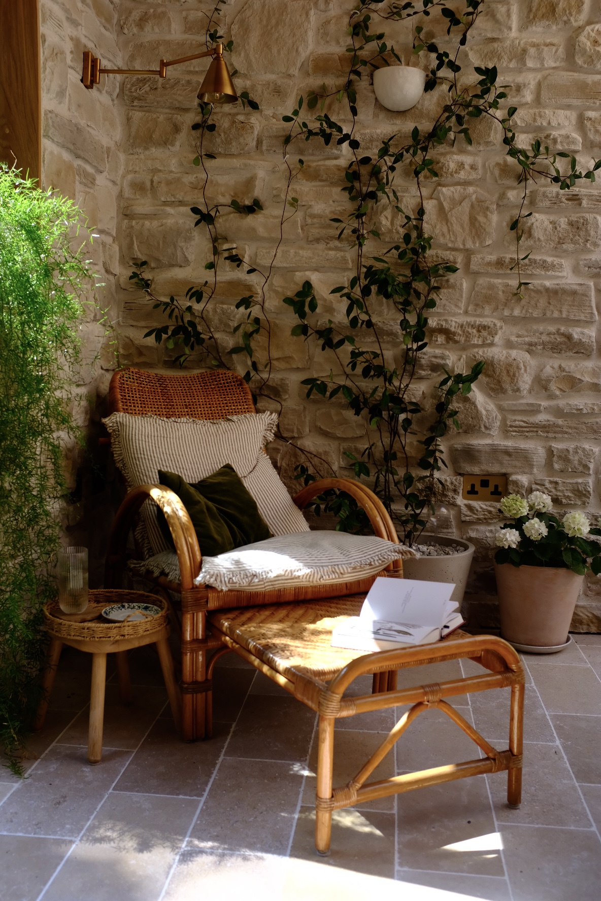 cane outdoor chair with matching footstool and cushions in the corner of an outdoor courtyard with vines and potted plants