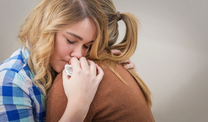 A teenage girl gets a warm hug from her mom.