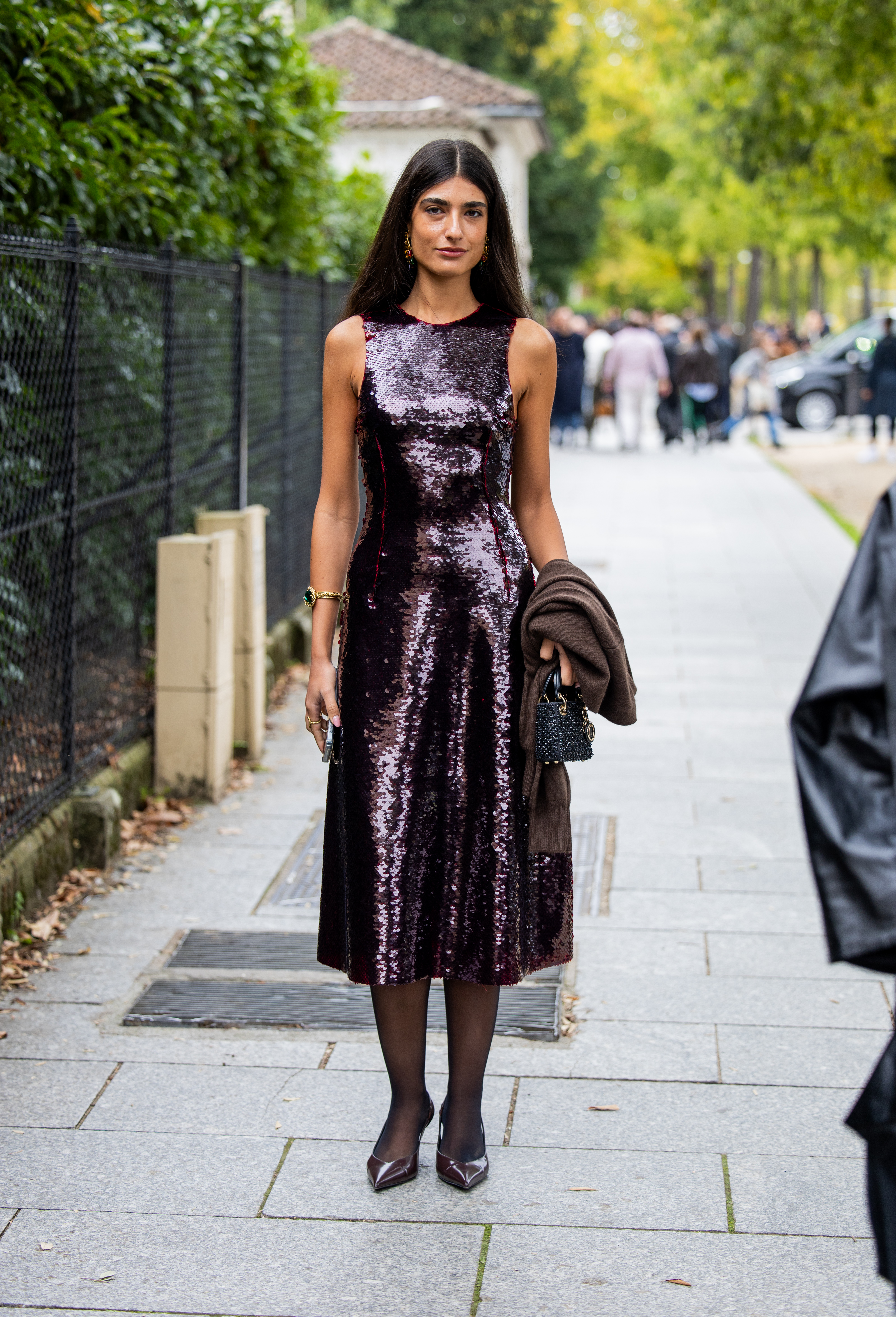 A woman wears a purple sequin dress, black sheer tights, and brown heels.