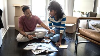 two females sat on floor in living room looking at magaines, papers and tablet