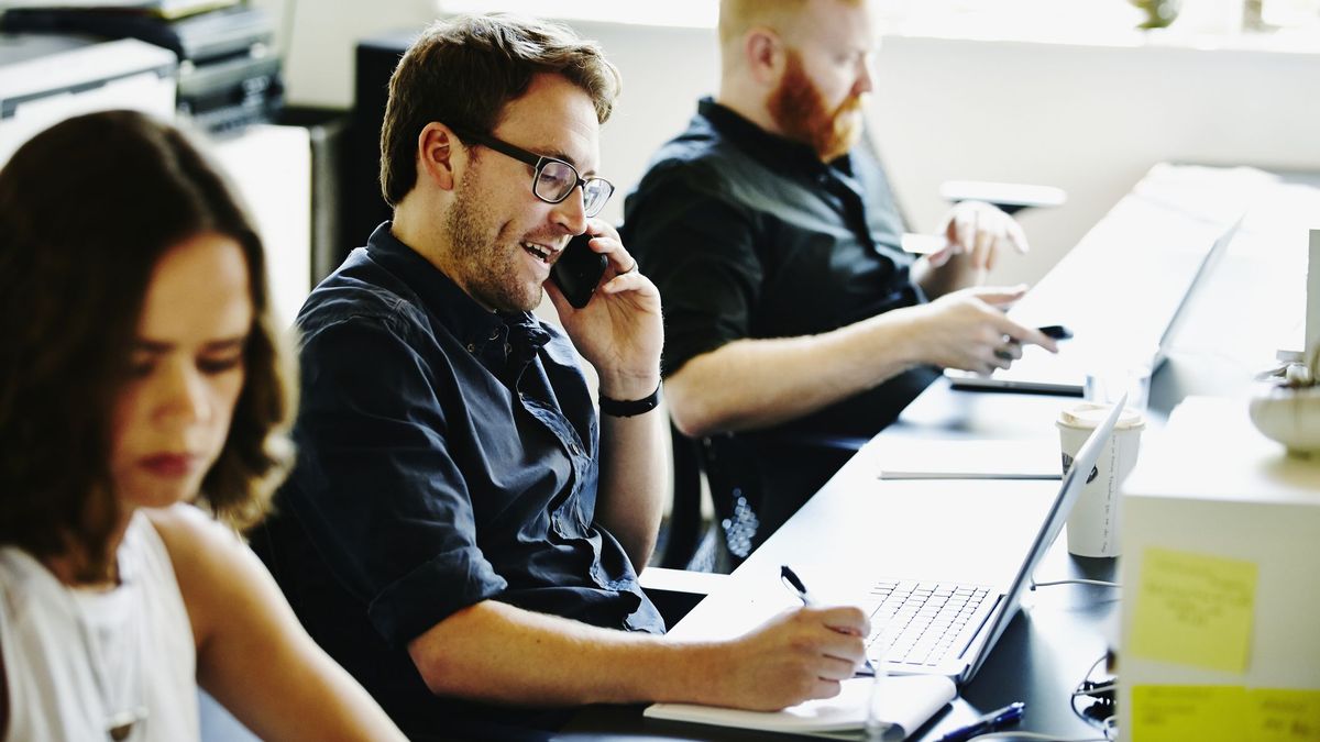 A man in an office using a mobile phone and writing on a notepad