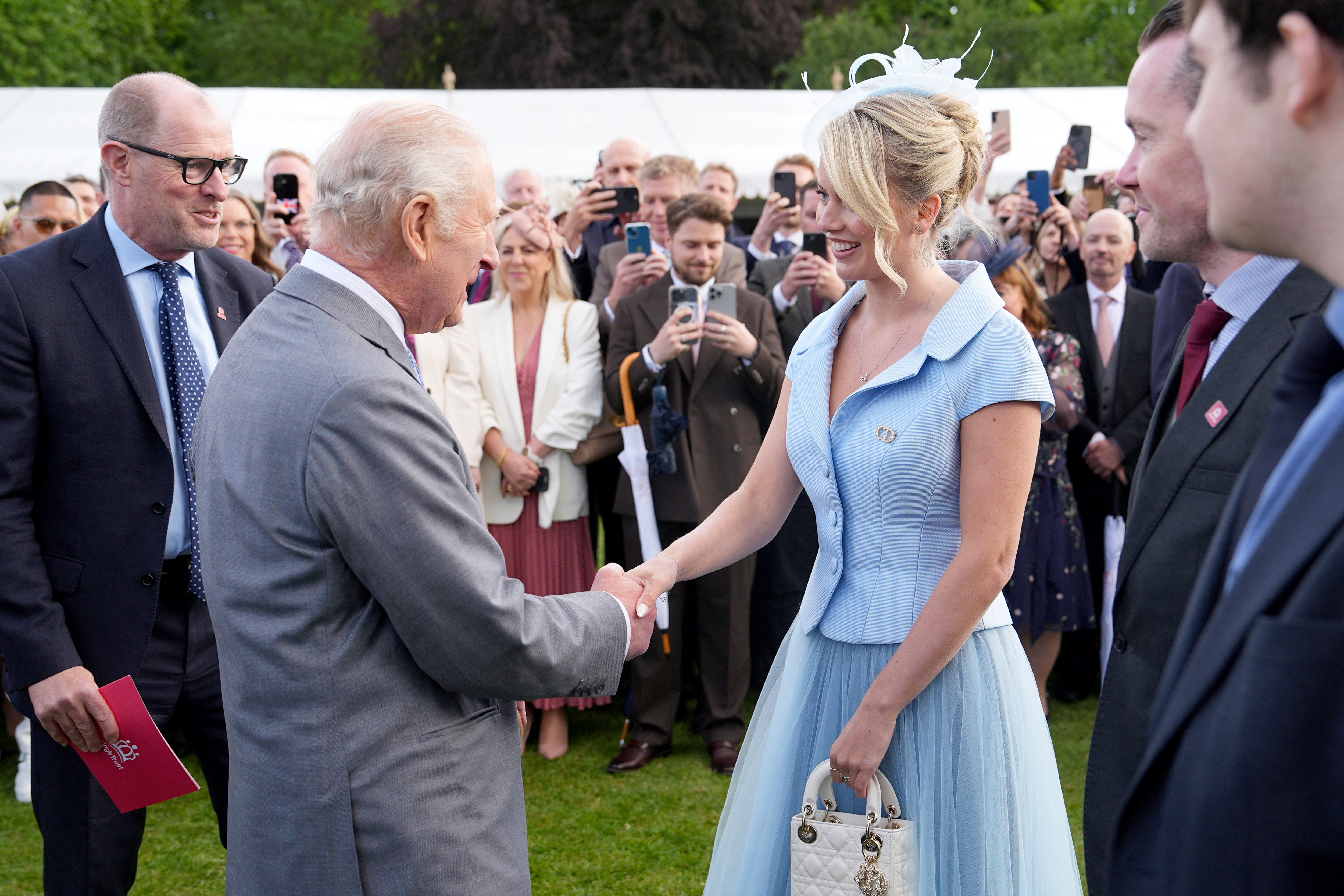 King Charles shaking hands with Tasha Ghouri at a garden party