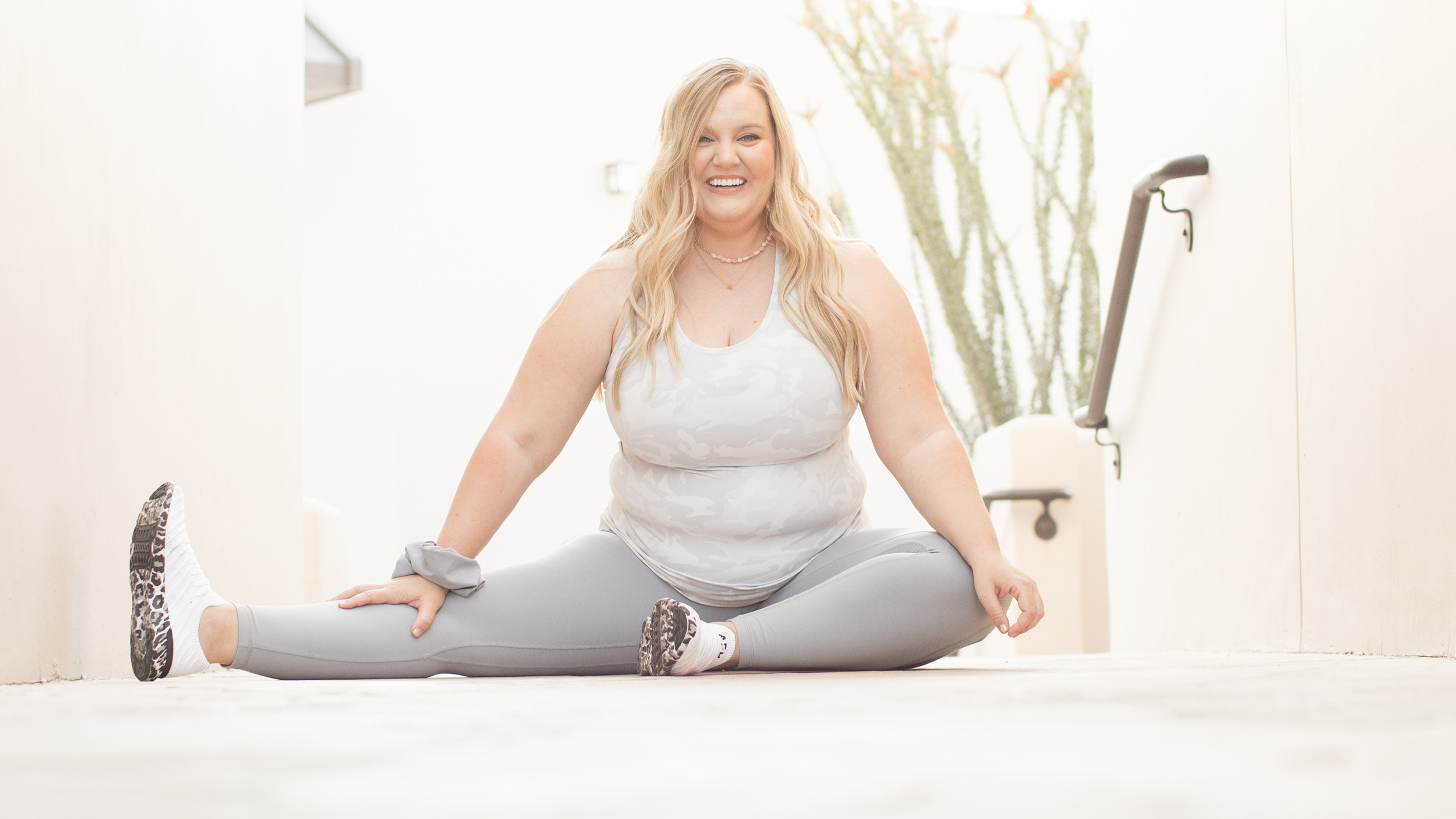Woman sitting on floor, smiling, with one leg extended to the side 