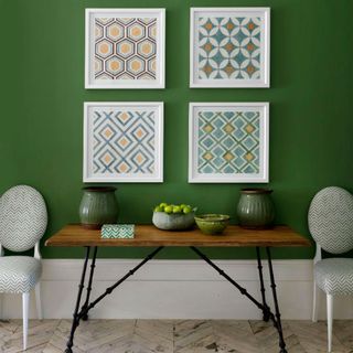green wall with white frames and wooden desk