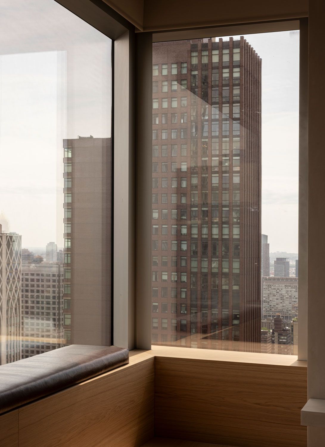 Built-in oak window seat at 262 Fifth Avenue by Norm Architects, set against corner glazing overlooking neighbouring Manhattan towers