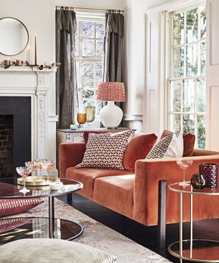 A living room curtain idea with orange velvet sofa and grey fold top curtains