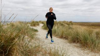 Woman in running gear moving over sand dunes in overcast weather