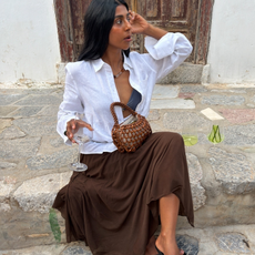 Influencer Monikh wearing a white linen shirt, brown asymmetric skirt and beaded bag. 