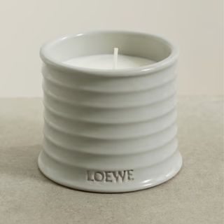 A small gray ribbed candle jar with LOEWE stamped into the bottom of it. A white wicked candle inside. 