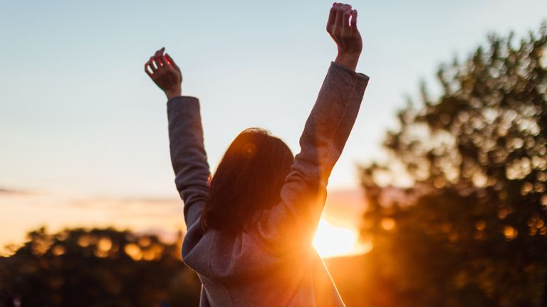 girl raising arms watching sunset meant to signify aries season and its fiery energy