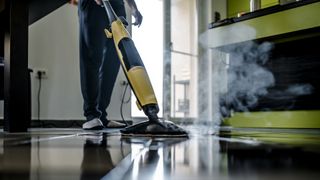 Person using a yellow steam mop to clean black tile floors with steam coming off.