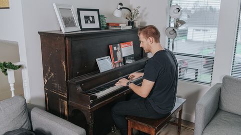 Man sits at his acoustic piano following a lesson on his tablet