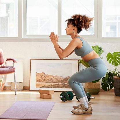 A woman doing a bodyweight squat in her living room at home