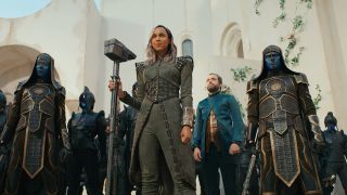 Still from The Marvels (2023) movie. Dar-Benn (shoulder length gray/light purple hair and wearing a grey outfit) is holding a large hammer/staff whilst standing in front of an army of Kree (blue humanoids).