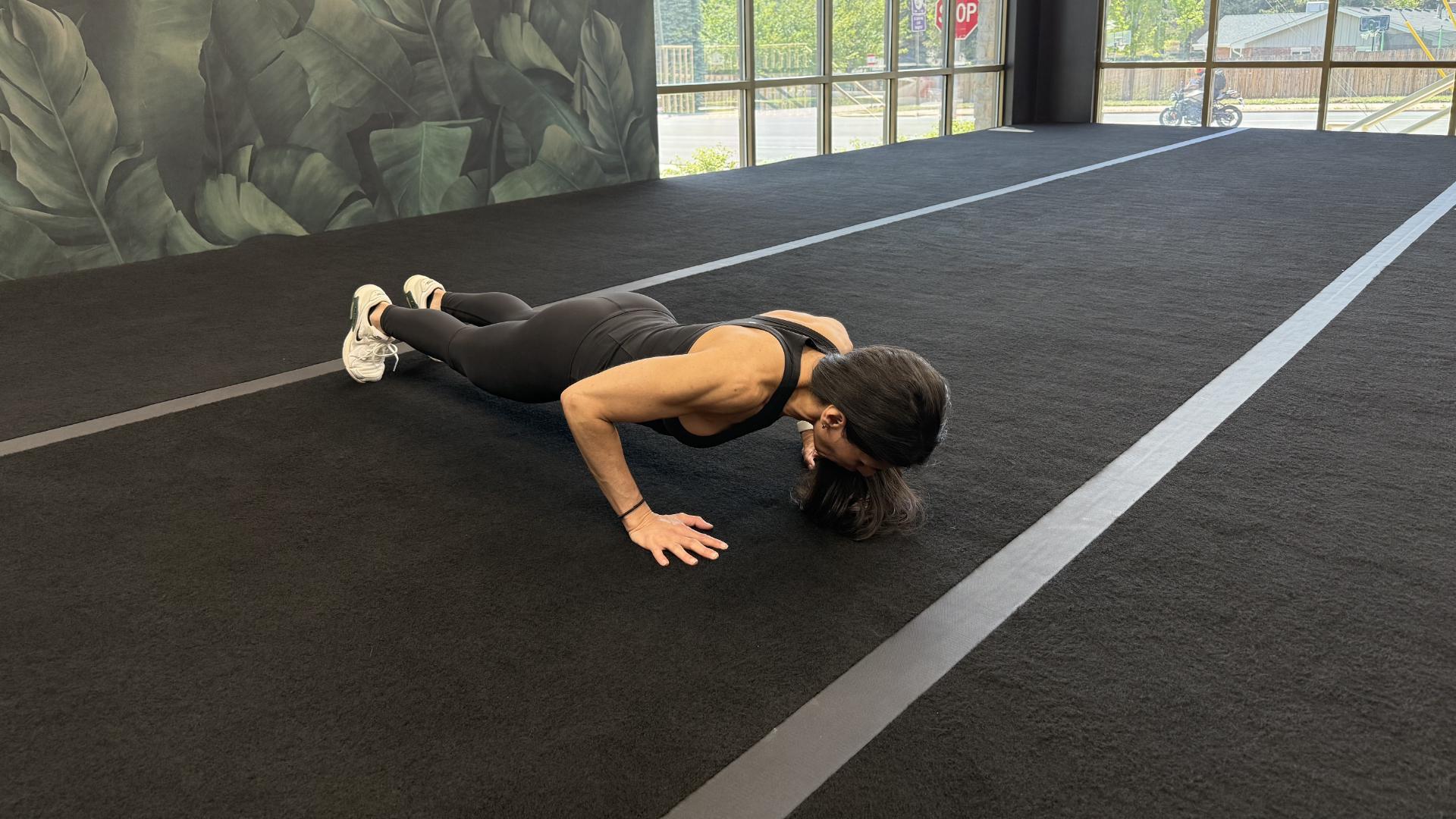 Woman exercising in empty gym space, performing a push-up on the floor