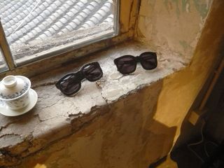 Two pairs of sunglasses and a china cup and saucer on an exposed brickwork windowsill