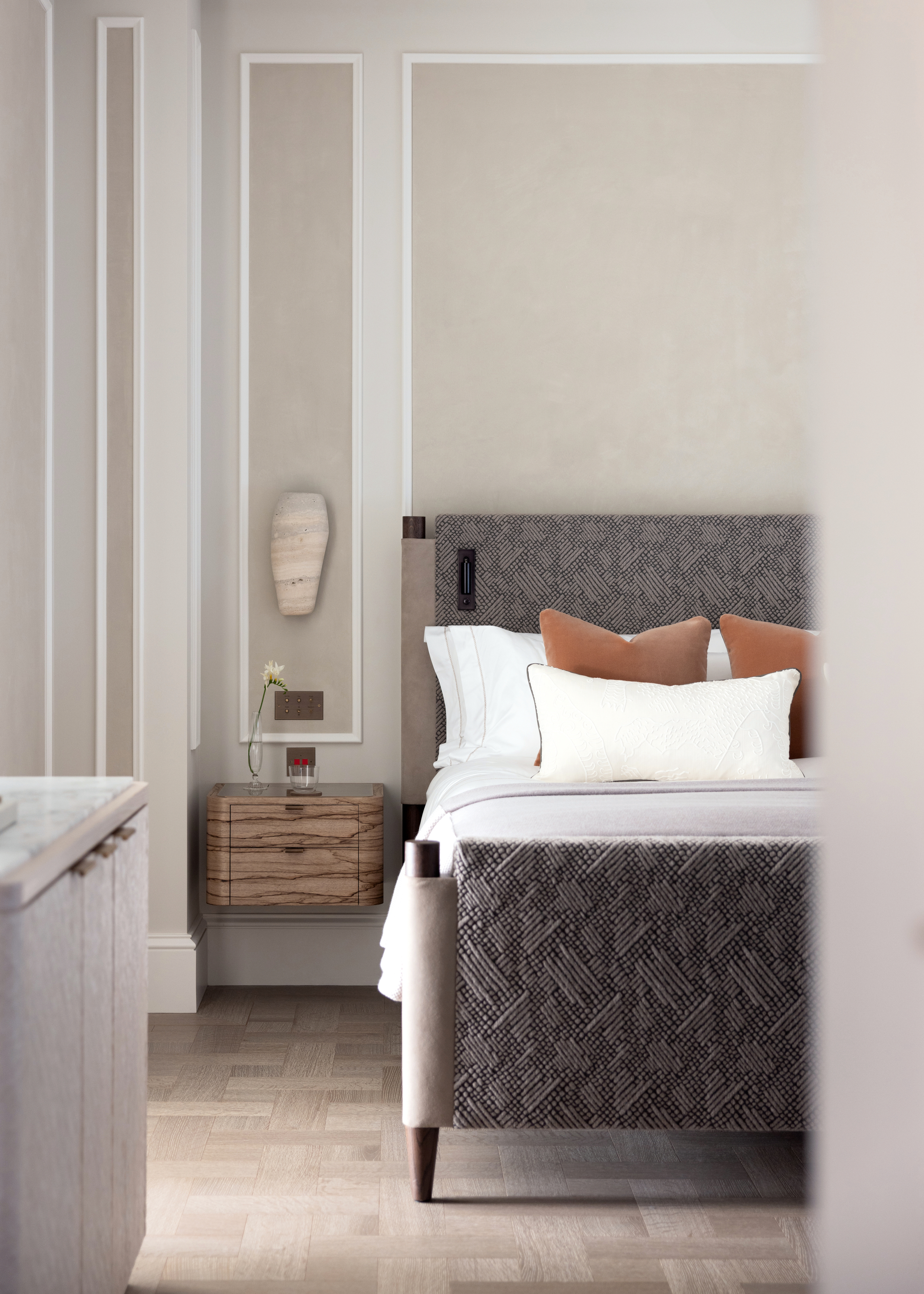 Bedroom with beige panelled walls, grey upholstered bed, wood bedside table and white bed linen