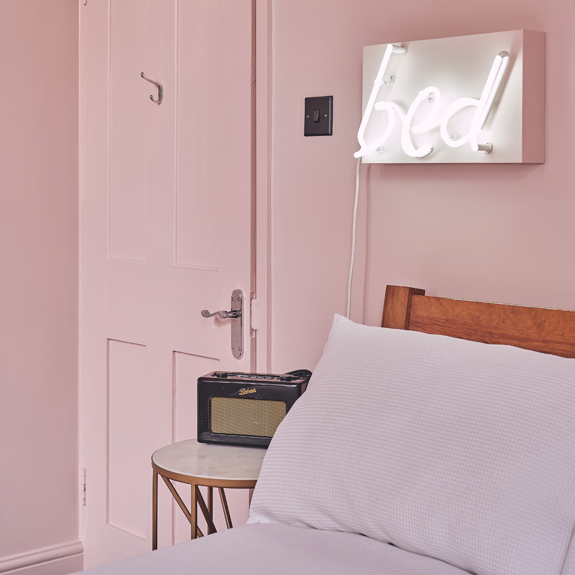 A colour-drenched pink bedroom with a neon light above the bed