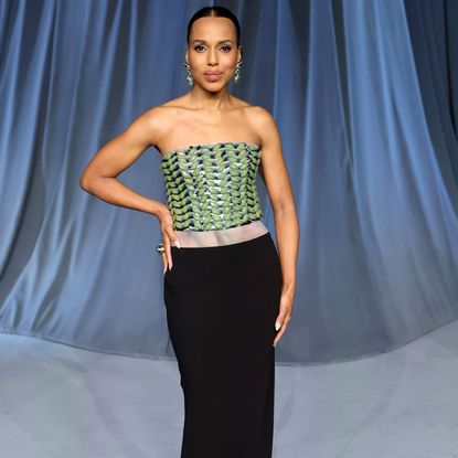 Kerry Washington wearing a slicked bun hairstyle and strapless gown. She has her hand on her hip and is smiling at the camera.