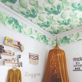 A kids room with storage shelves on the wall and a cactus-print wallpaper on the ceiling