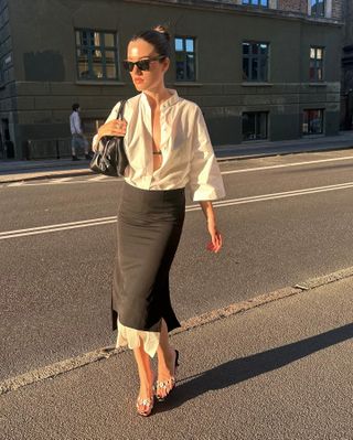 @iliridakrasniqi wearing a white button-down shirt tucked into a double-layer black pencil skirt with sandals and a black purse.