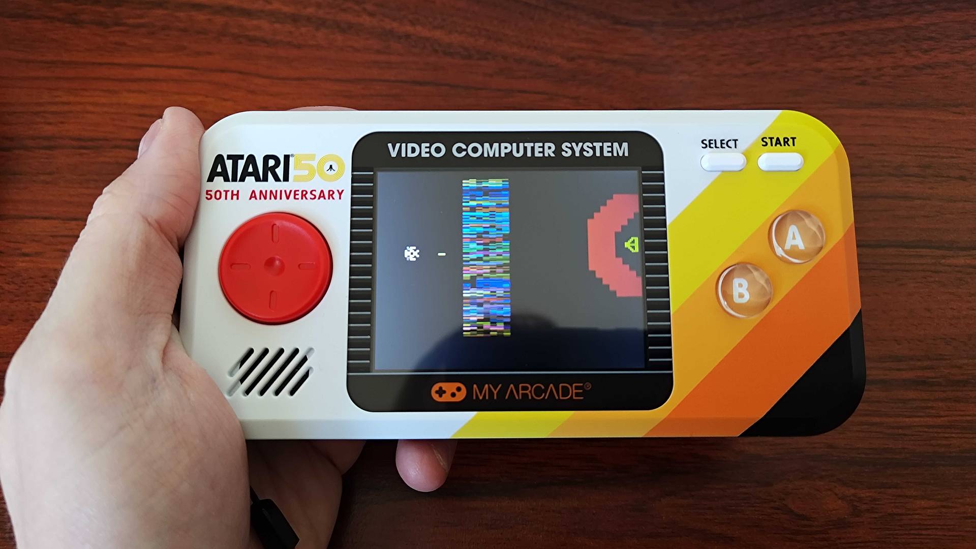 Hand holding Atari Pocket Player Pro with Yar's Revenge gameplay on screen.