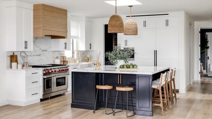 White kitchen with blue island, black and wood bar stools and rattan pendant lights