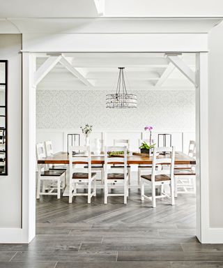 A dining room with neutral patterned wallpaper and rustic white and wood table and chairs
