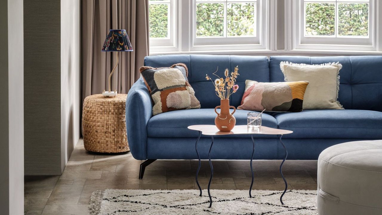 Blue sofa with cushions in front of large windows in living room, coffee table, ottoman