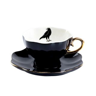 A black teacup with a white interior with a raven illustration