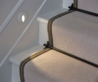 white staircase with stair lights and cream braided stair runner and stair rods