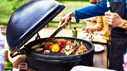 person cooking meant and vegetables on a large egg-style BBQ